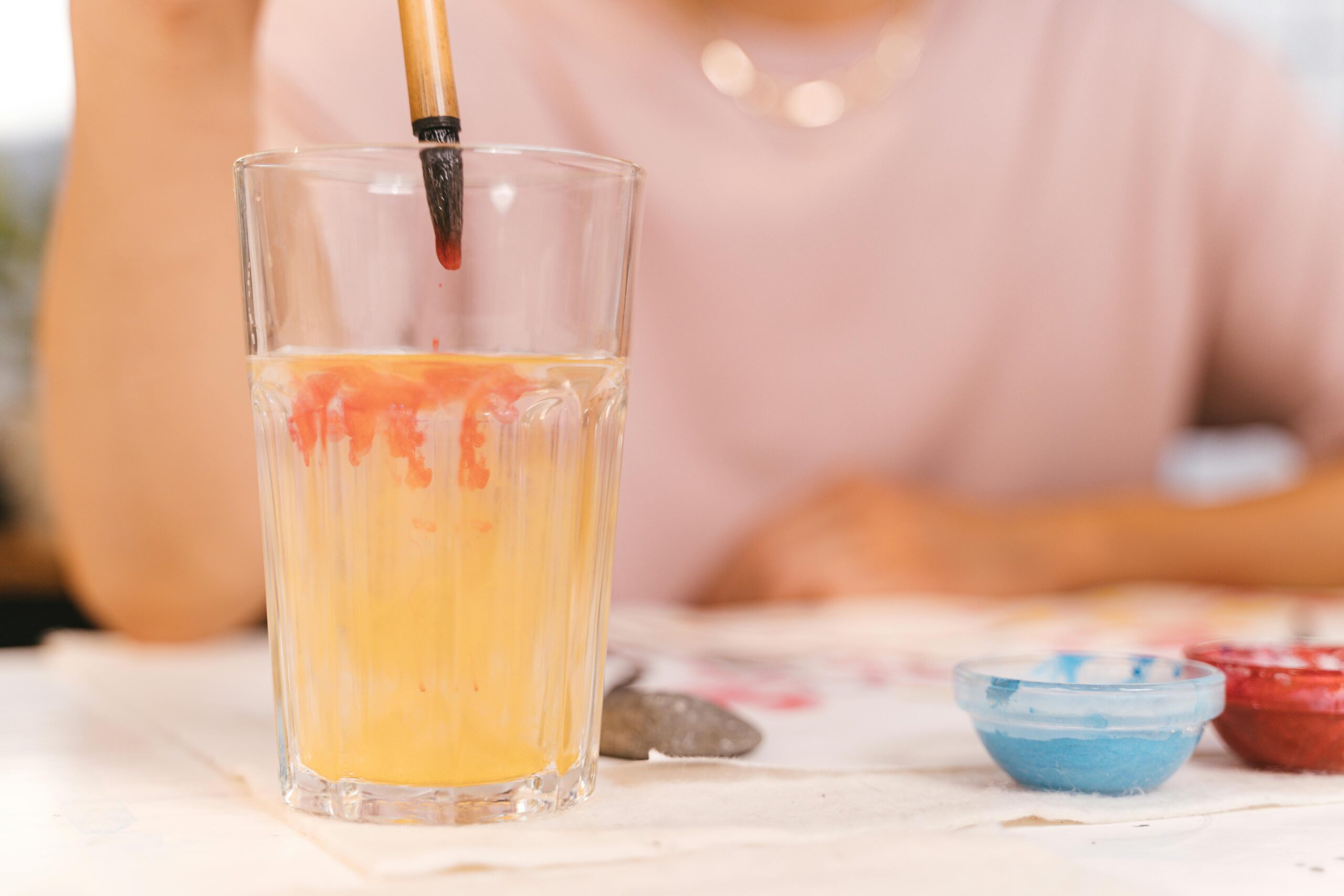 A close-up image of a paintbrush dipping into a glass of water, mixing vibrant watercolors.